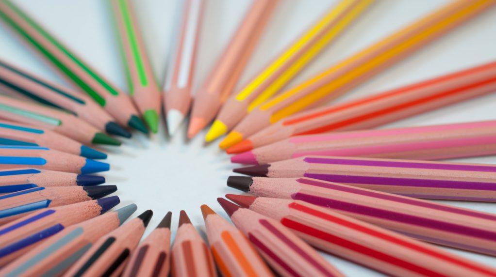 Colored pencils aligned in a spiral on a white table.