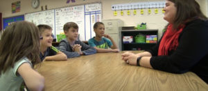 A teacher speaking with a group of students at a table in the classroom.
