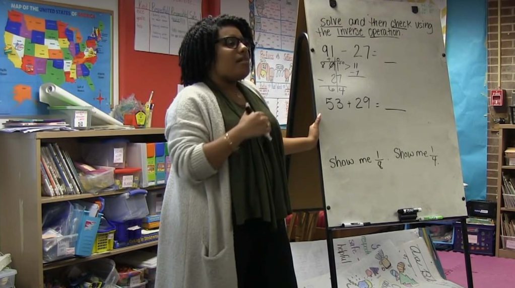 A teacher speaking in front of a whiteboard.