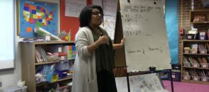 A teacher speaking in front of a whiteboard.