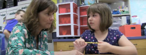 A teacher speaking with a students in a classroom.